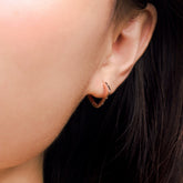 Fine jewellery, silver jewellery plated with rose gold, hypoallergenic, tarnish-free, close-up side view of a rose gold hoop earrings with crystals worn on a person's ear